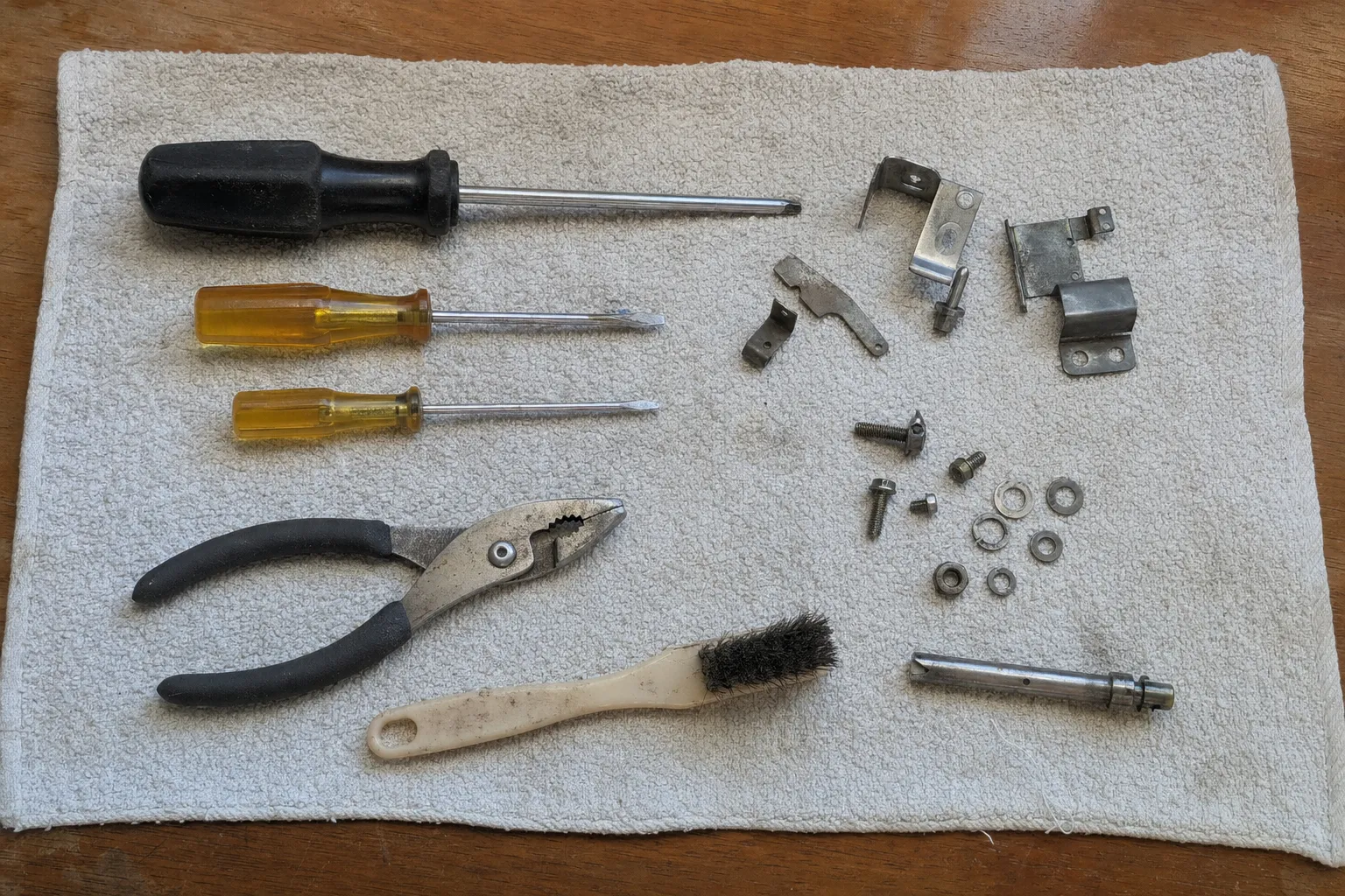 Hand tools on a service towel with removed hinge brackets, a latch shaft, screws, nuts and washers in rows